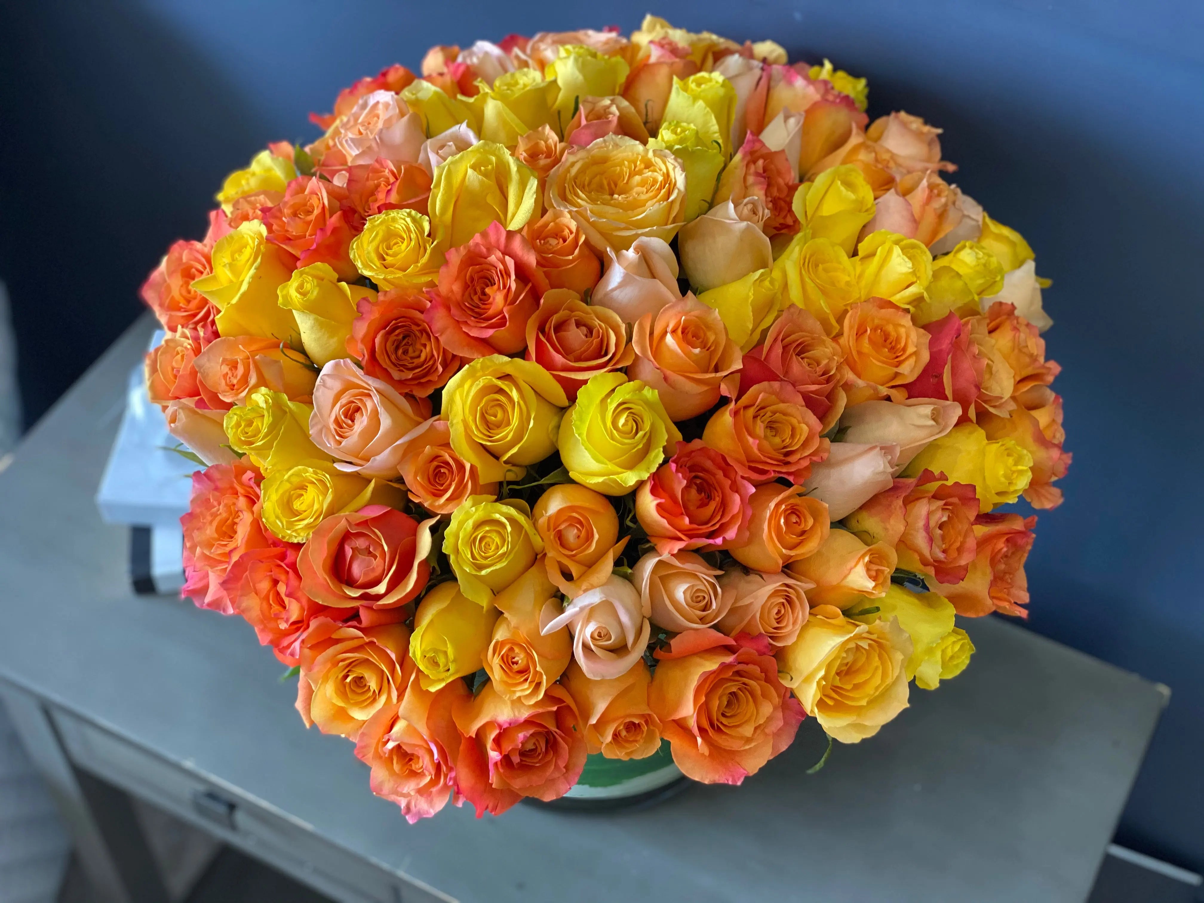 100 colorful roses arranged in a lush rounded floral design