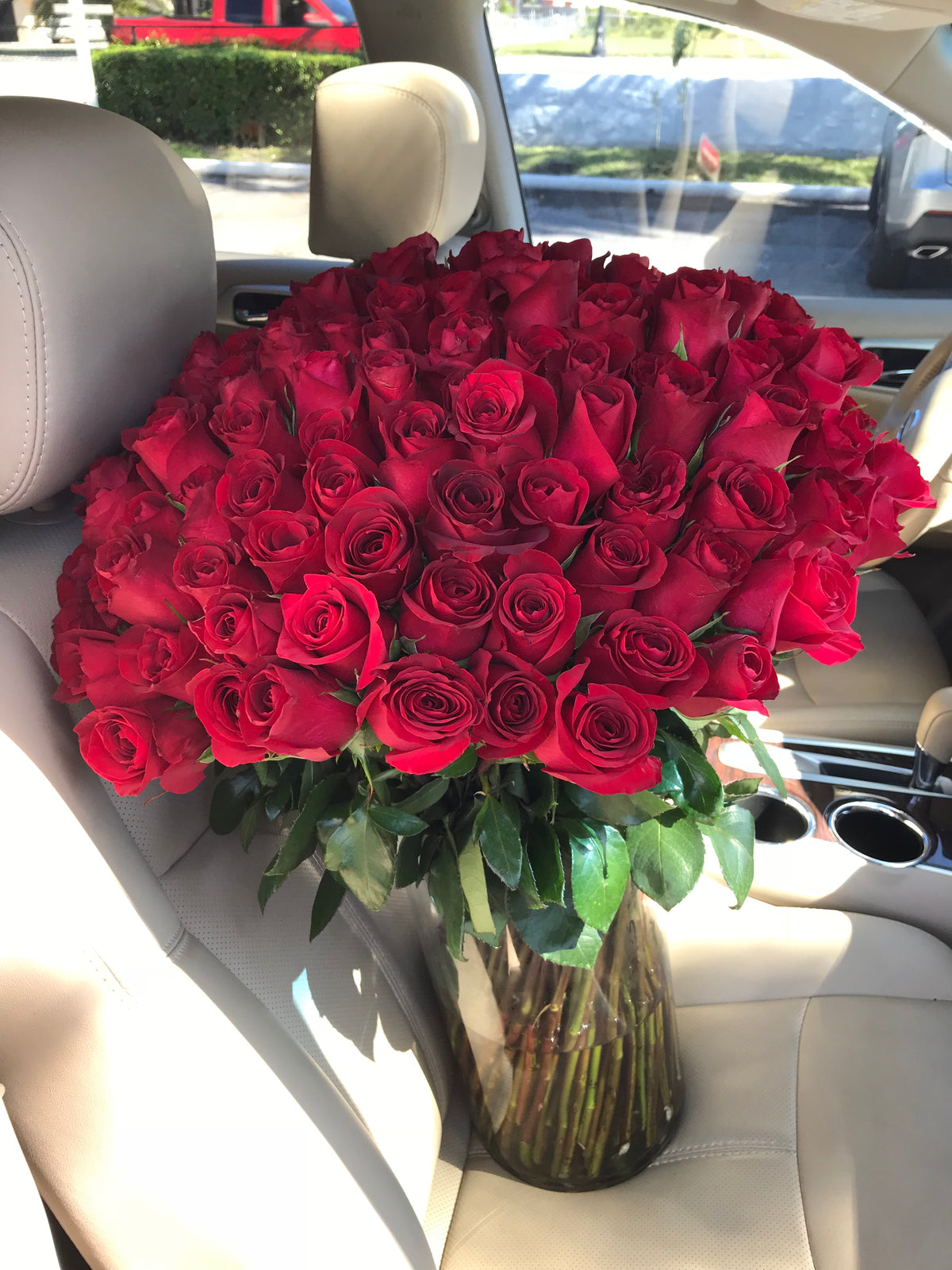 100 premium red roses arranged in tall clear glass vase