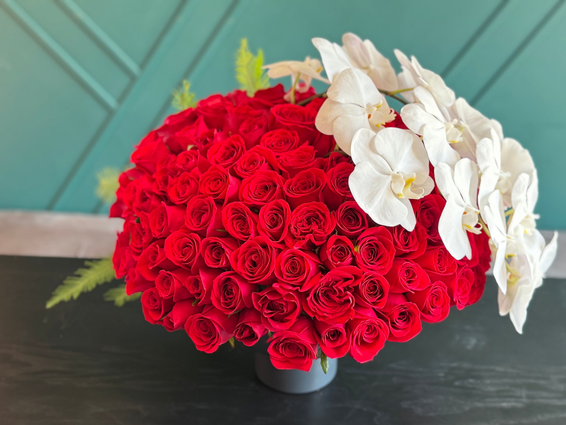 150 red roses Miami arrangement with white phalaenopsis orchids in black metal vase
