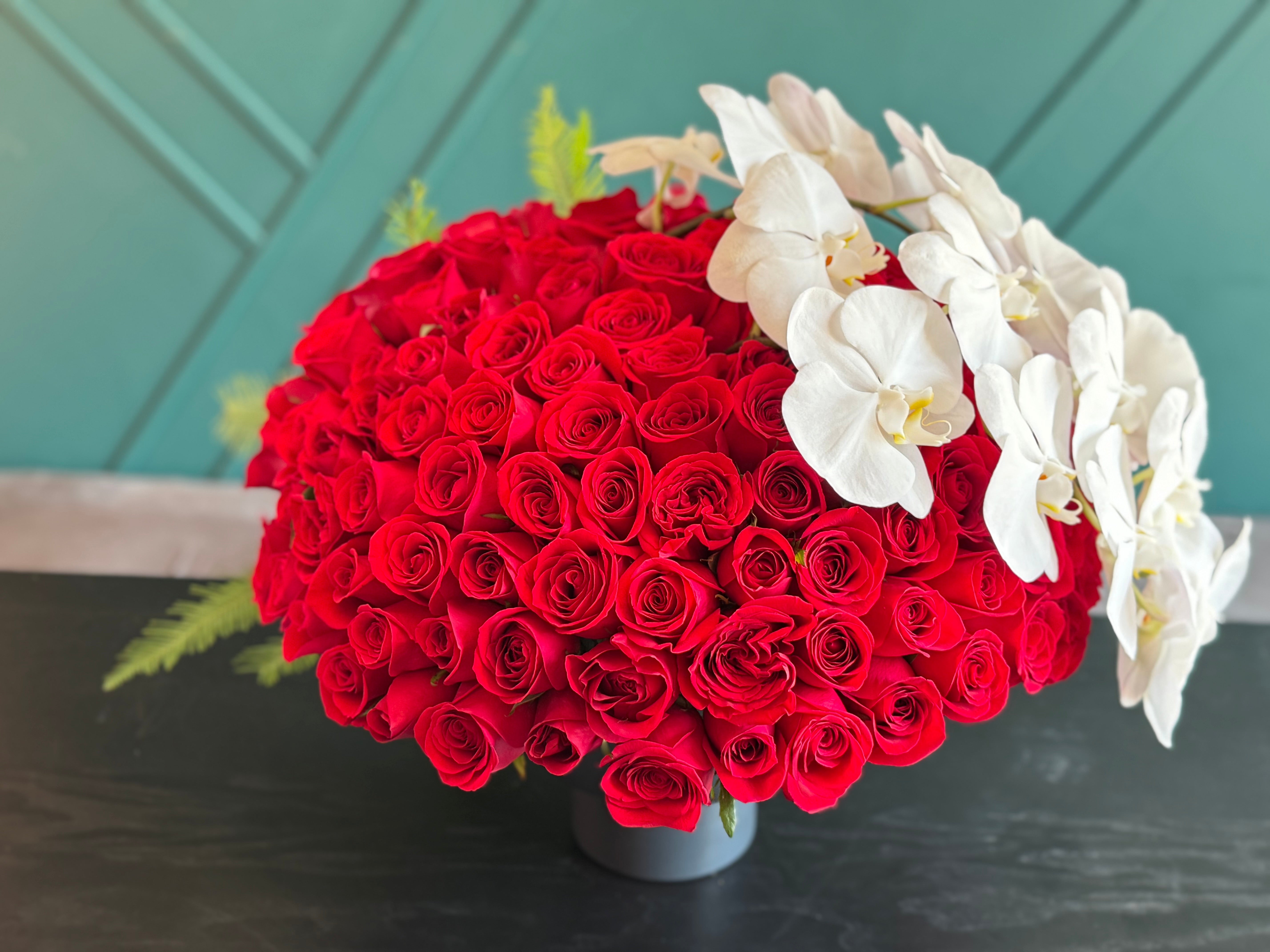 150 red roses Miami arrangement with white phalaenopsis orchids in black metal vase
