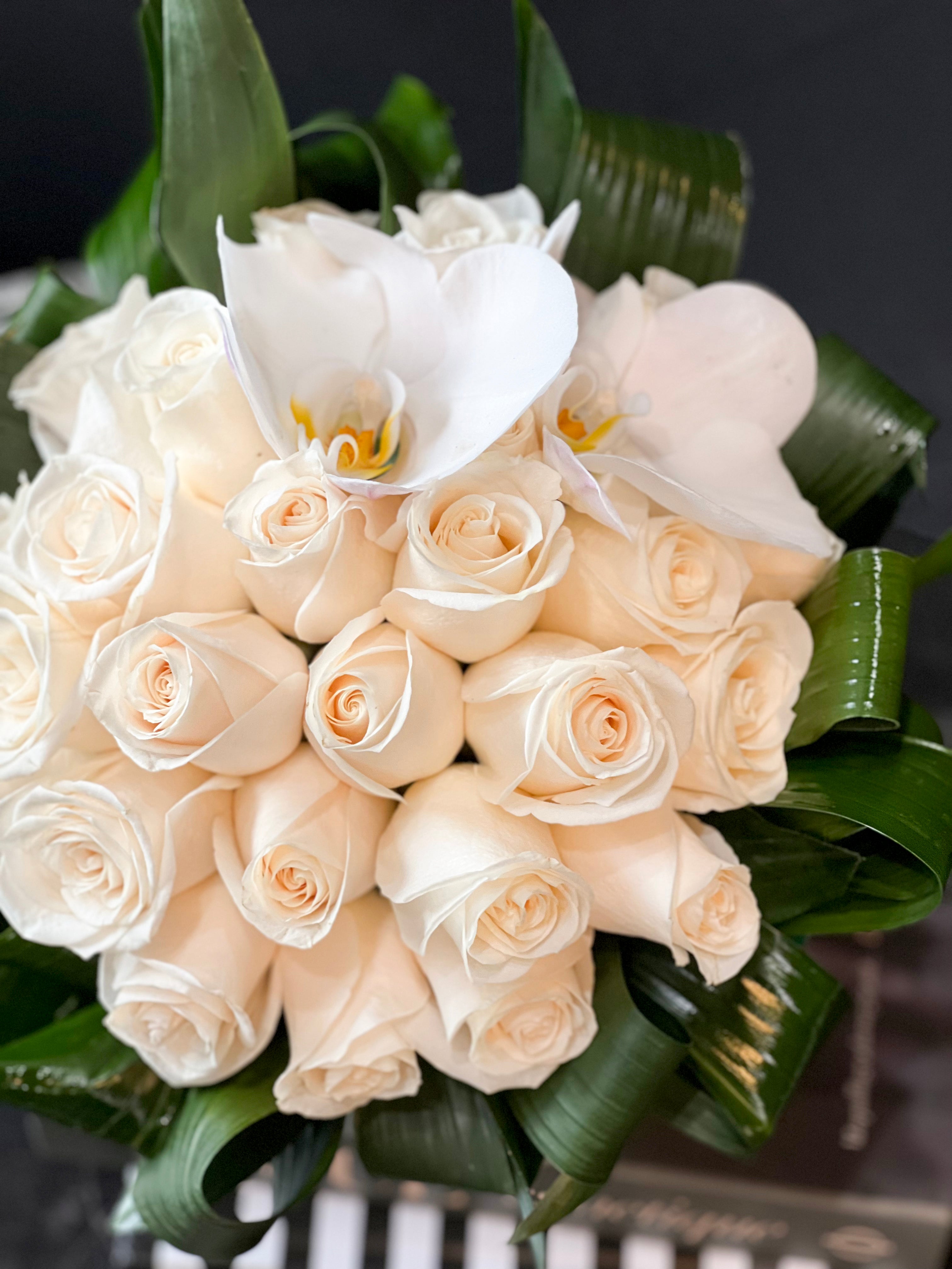 24 fresh white roses in a fishbowl vase with greenery accents