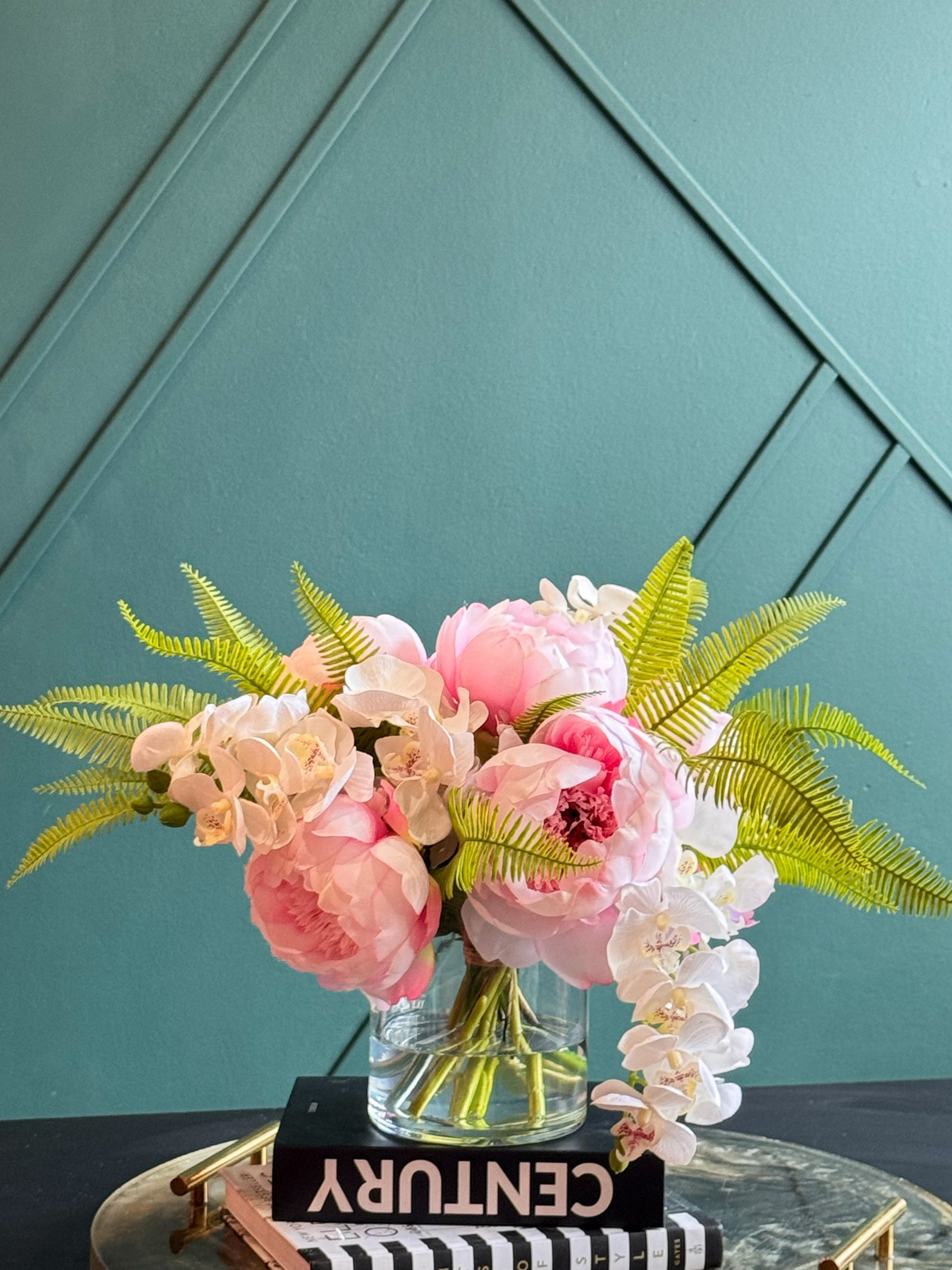 Artificial pink peonies and white orchids arranged in a clear vase with realistic greenery.