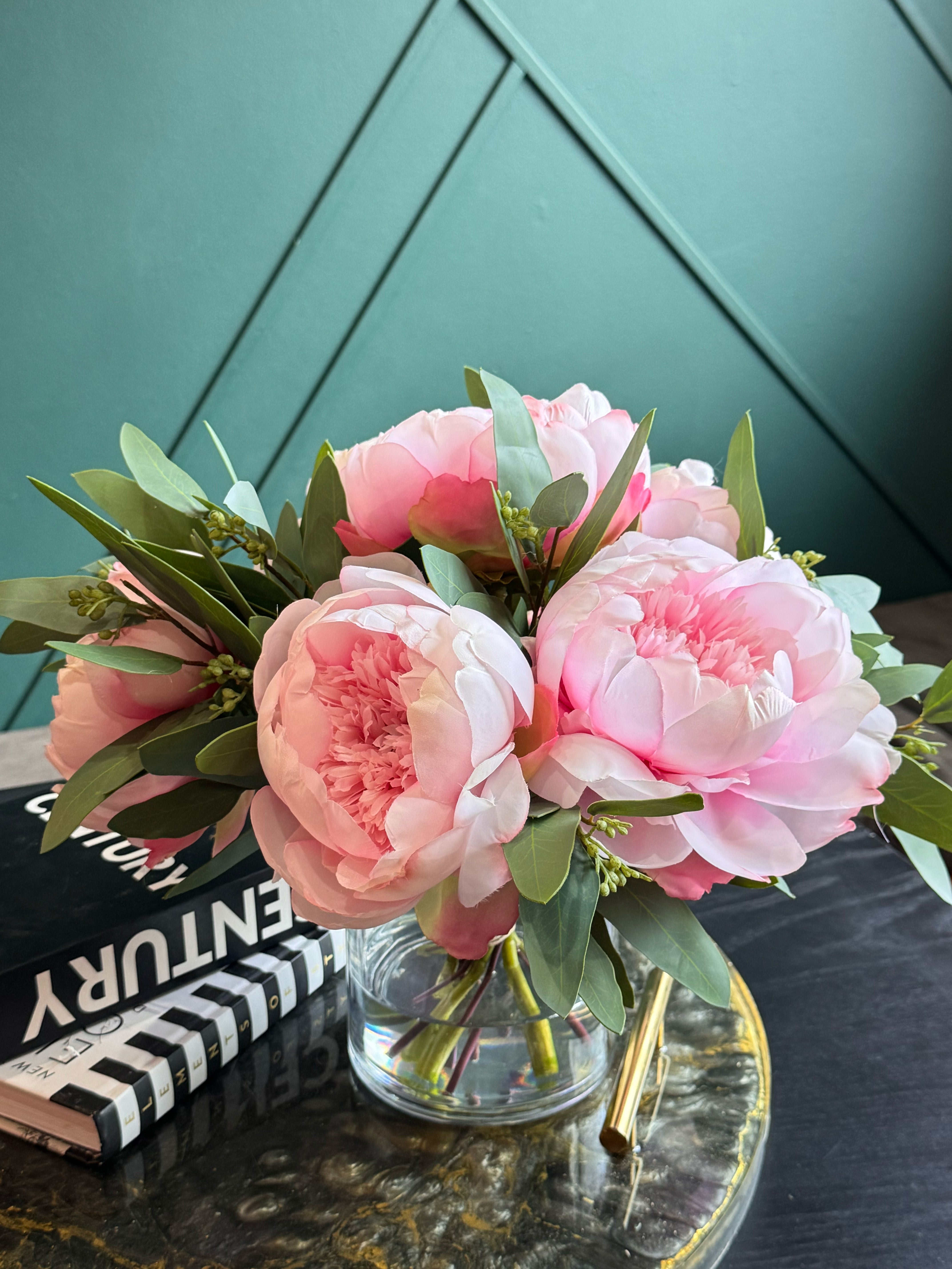 Artificial pink peonies in a clear glass vase creating a timeless floral centerpiece.