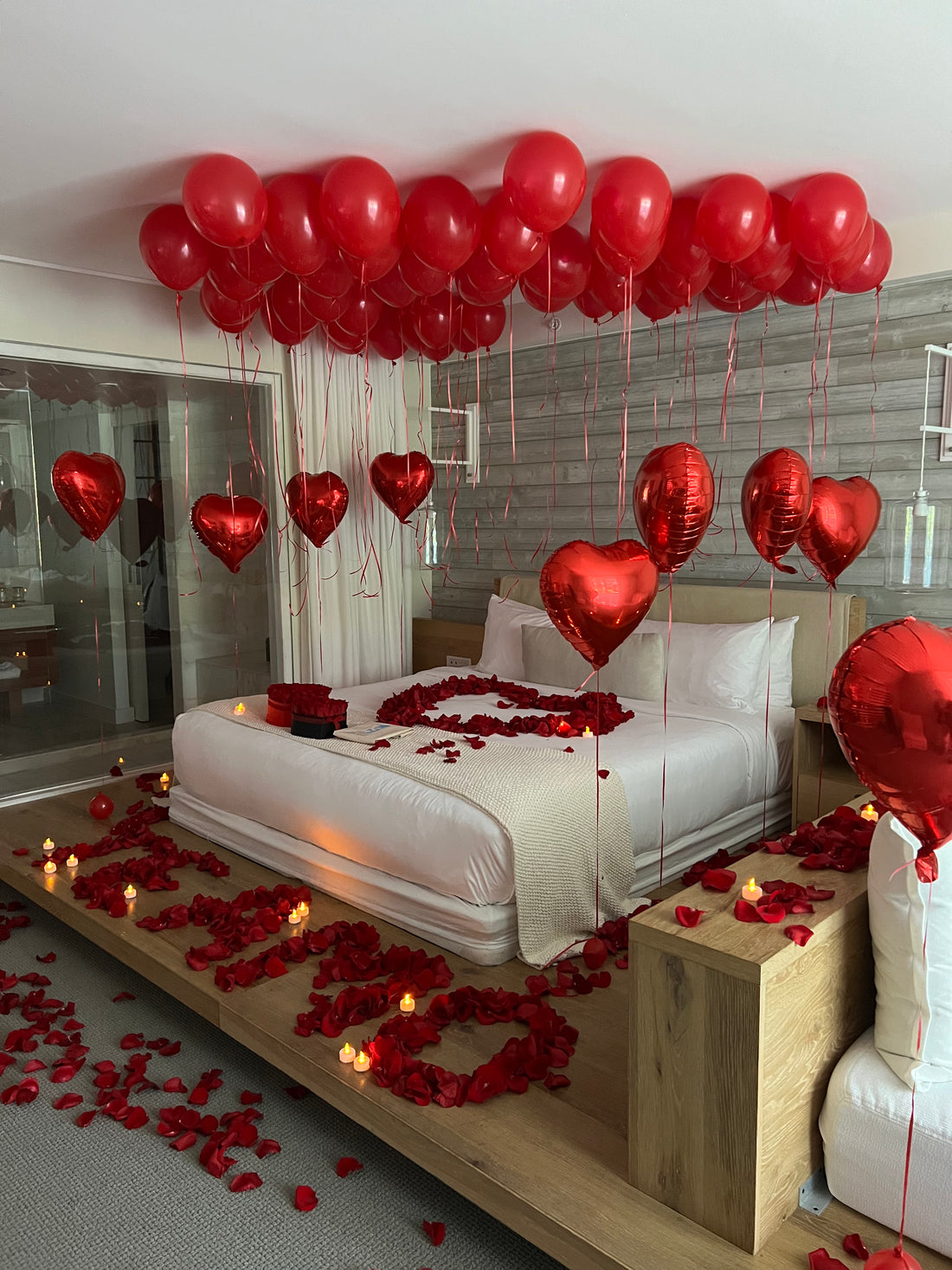 Luxury romantic room setup in Miami with red heart balloons and rose petals