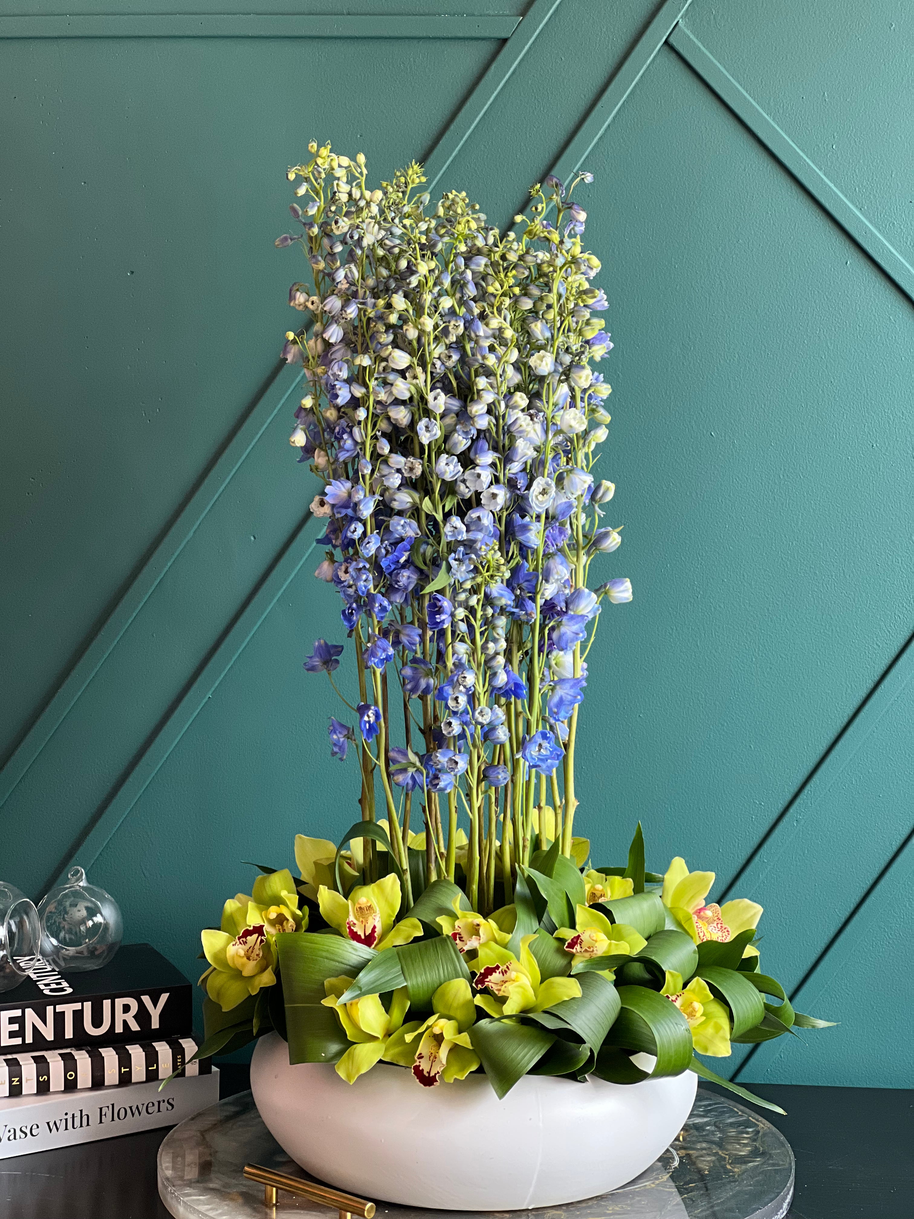 Modern flower arrangement with tall blue delphinium and orchids