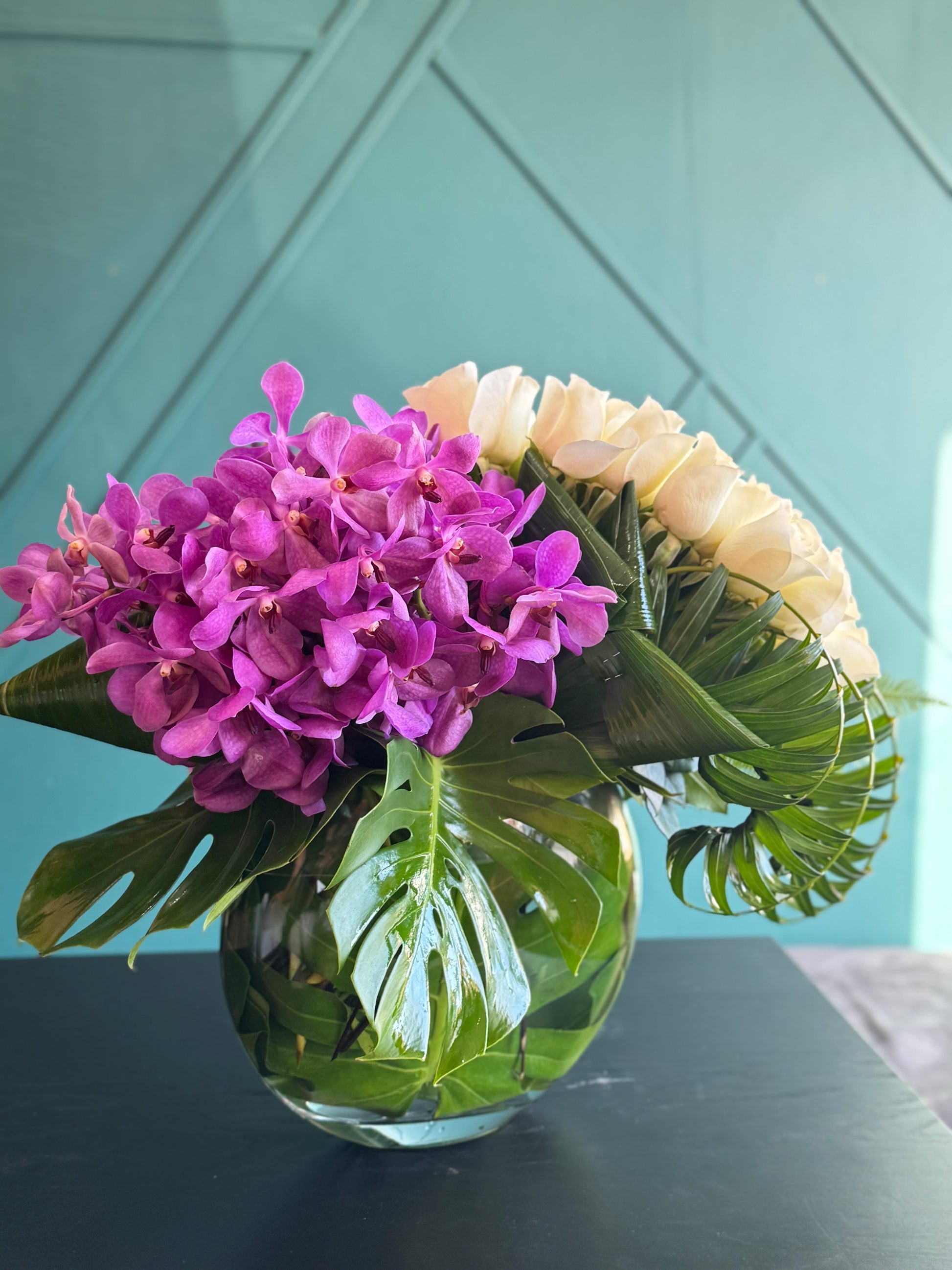 Modern flower arrangement with white roses Mokara orchids and tropical leaves