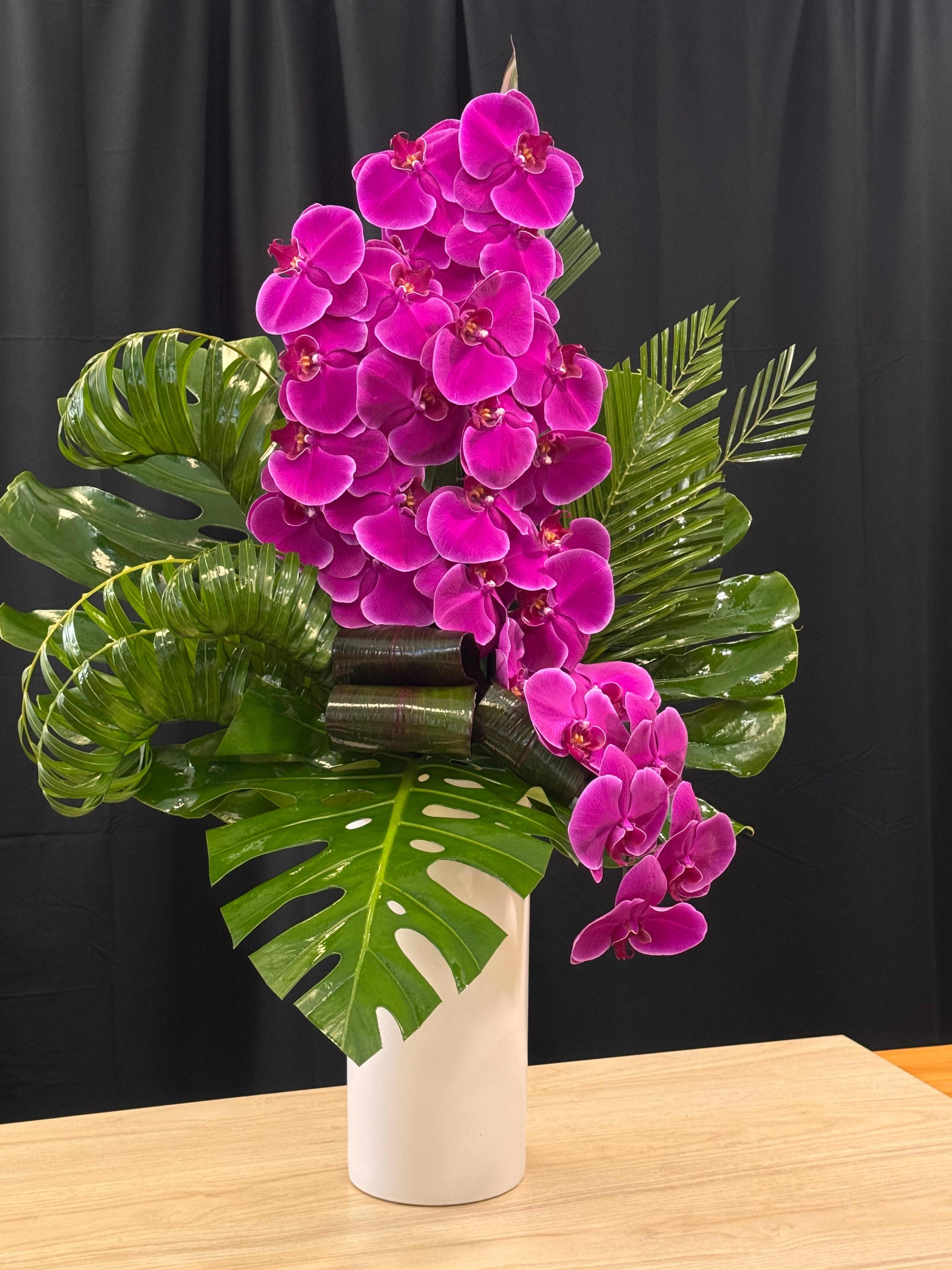 Purple phalaenopsis orchids arranged with lush green tropical leaves