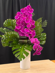 Purple phalaenopsis orchids arranged with lush green tropical leaves