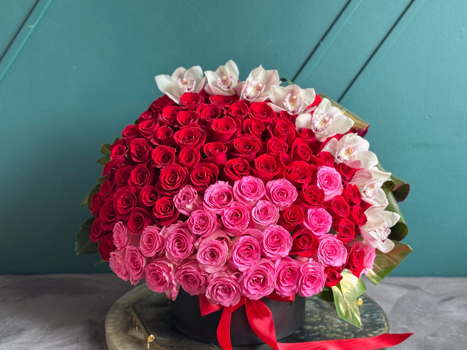Red and pink roses in round flower box with cymbidium orchids