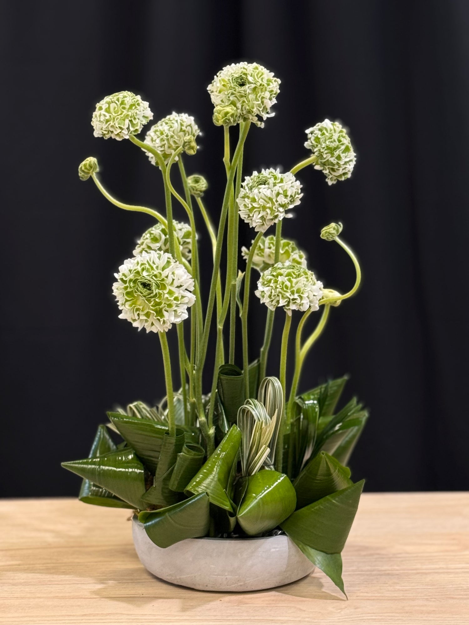 Stylish ranunculus flowers in a modern vase with tropical greenery