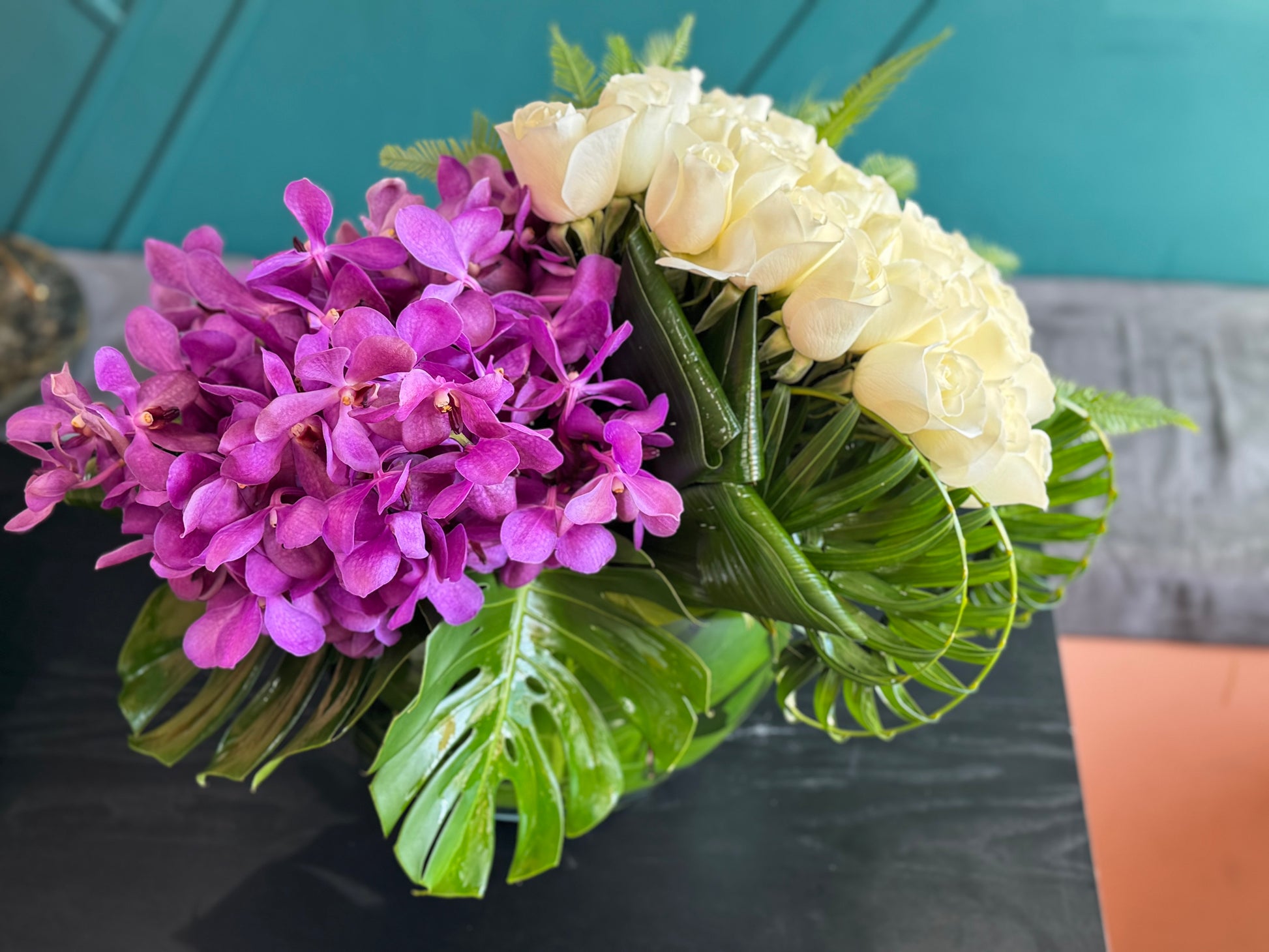 White roses with purple Mokara orchids and tropical greenery in moon vase