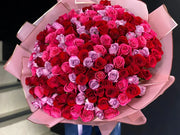 Bouquet of red, pink, and purple roses in a pink paper wrap.