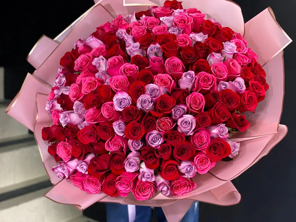 Bouquet of red, pink, and purple roses in a pink paper wrap.